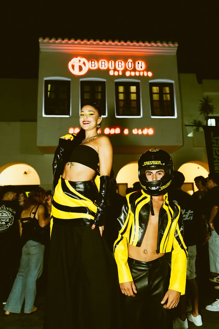 Dos artistas vestidas de amarillo y negro delante de la fachada de Bribón del Puerto.