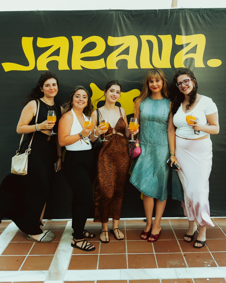 Cinco amigas con copa posan delante del cartel de JARANA.
