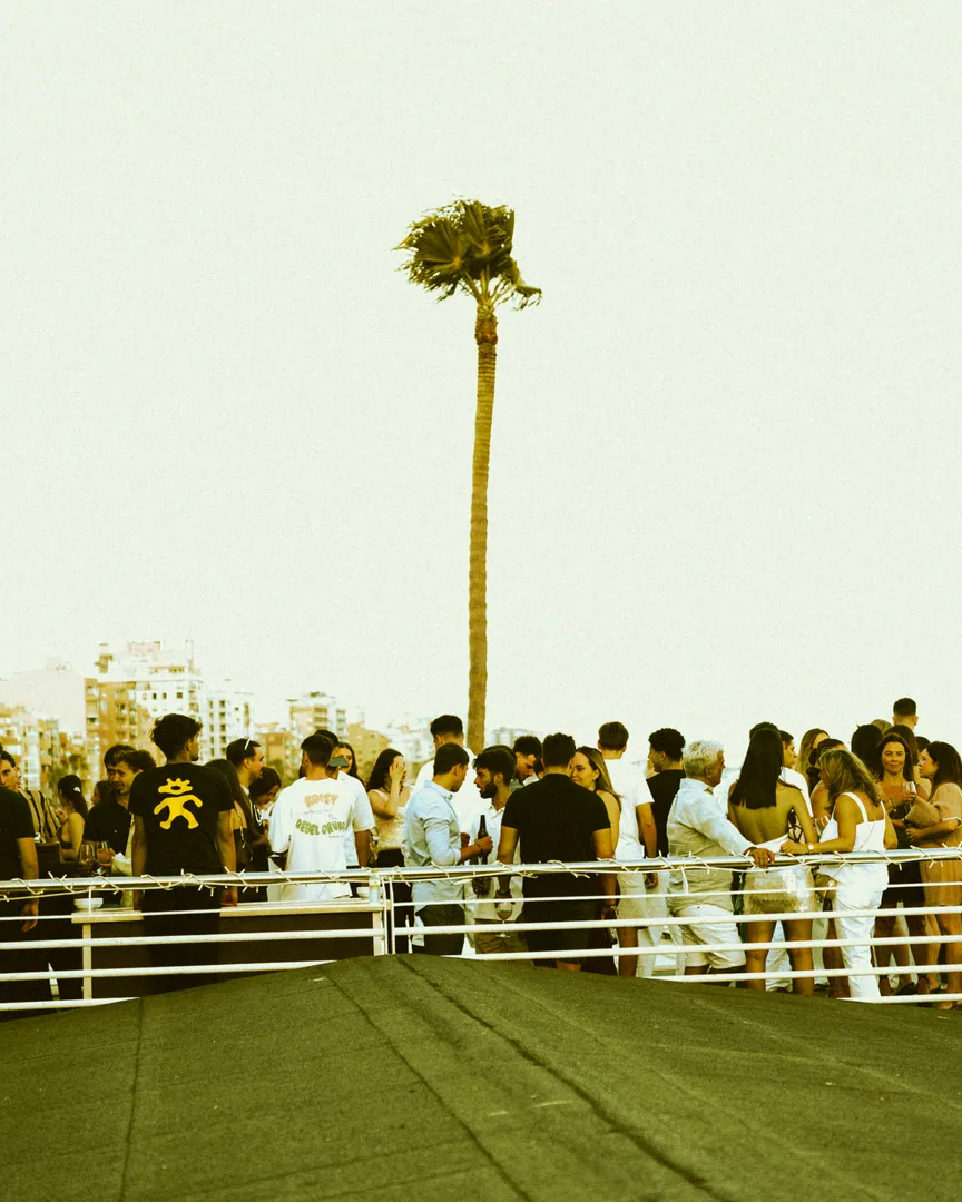 Gente en la terraza de El Candelero con luz de día y una palmera.