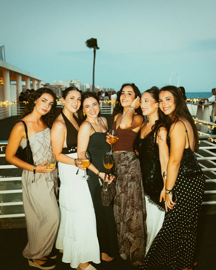 Seis amigas brindan en la terraza de El Candelero, con el mar detrás.